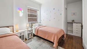 Een slaapkamer met twee bedden, een raam, een bureau en een dressoir.