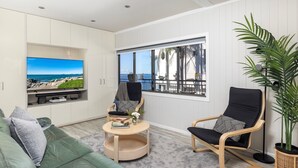 A modern living room with a large TV, comfortable seating, a small table, and a view of the ocean.