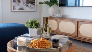 Une table à manger avec des gaufres, une bouteille de champagne Minchinbur Classic Brut, une bougie et un pot de beurre de cacahuète biologique.