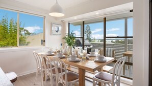 Un coin repas avec une table en bois dressée pour quatre personnes, des chaises blanches et une vue sur l’extérieur.
