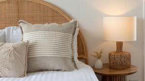 Un lit avec une tête de lit en osier, une lampe de chevet et des coussins décoratifs.