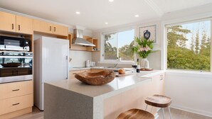 Une cuisine moderne dotée d’un grand îlot central, d’appareils électroménagers intégrés et offrant une vue sur l’extérieur.
