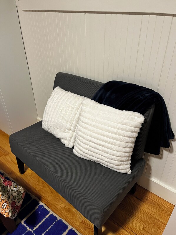 A small, dark grey sofa with a white, textured throw blanket and a dark blue blanket draped over it.