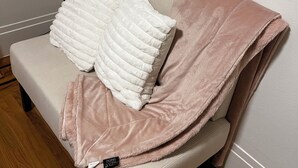 A sofa with a white cushion and a pink blanket, positioned against a plain wall with wooden flooring. - Charming, private 3BR cottage with WiFi, A/C, full washer & dryer in Oakland (Oakland)