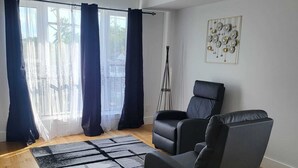 Una sala moderna con un sofá de cuero negro, un tapete blanco y negro y un ventanal con cortinas.
