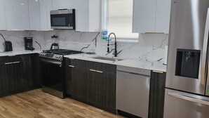 Una cocina moderna con armarios blancos, un refrigerador de acero inoxidable, un microondas, un fregadero y un lavavajillas.
