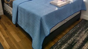 Una cama bien hecha con un colcha azul, una almohada y una toalla doblada sobre la cama.