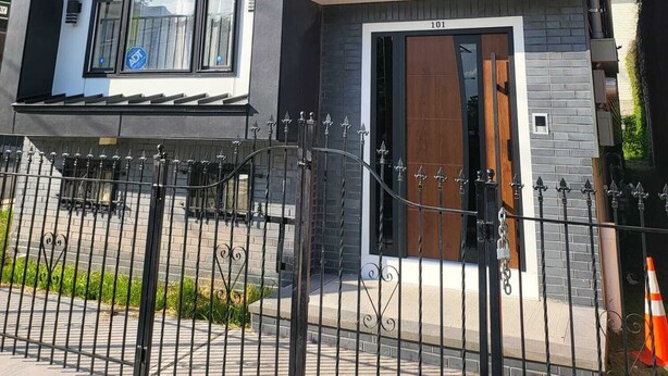 Un edificio moderno de dos pisos con ventanas grandes, una puerta visible y una valla metálica en primer plano.