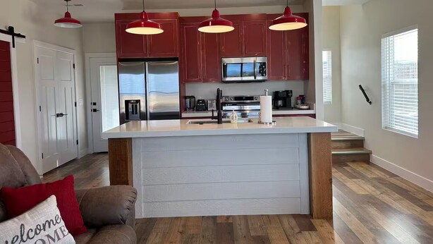 A modern kitchen with red cabinets, stainless steel appliances, and pendant lighting.