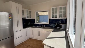Une cuisine moderne avec des meubles blancs, un réfrigérateur en acier inoxydable, un plancher en bois et une fenêtre qui laisse entrer la lumière naturelle.