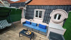 Una terraza en la azotea con un sofá de mimbre, una mesa de comedor y una bandeja de comida, además de un césped verde.