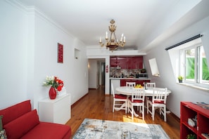 A dining area with a white table and chairs, a chandelier, and a red bookshelf.