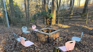 A fire pit surrounded by four chairs in a wooded area.