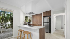 A modern kitchen with a large island, wooden cabinets, and stainless steel appliances. There are two bar stools and a view of the outdoor patio.