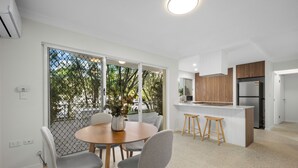 A modern kitchen with wooden cabinets, a stainless steel refrigerator, and a dining area with a round table and grey chairs.