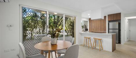A modern kitchen with wooden cabinets, a stainless steel refrigerator, and a dining area with a round table and grey chairs.