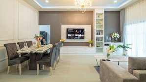 A modern living room with a dining area, a TV mounted on the wall, and a chandelier. - Villa Anna (Pattaya)