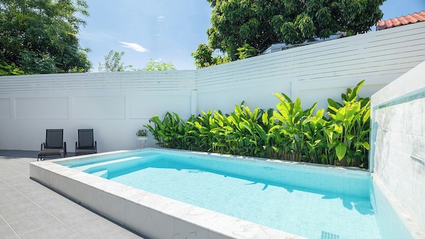 A rectangular swimming pool with a tiled edge, surrounded by a white wall and lush green plants. - Villa Anna (Pattaya)