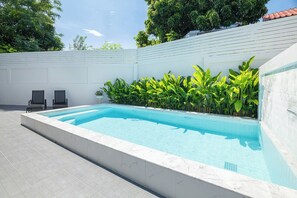 A rectangular swimming pool with a tiled edge, surrounded by a white wall and lush green plants. - Villa Anna (Pattaya)