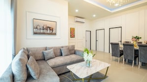 A modern living room with a grey sectional sofa, a marble coffee table, and a dining area with grey chairs and a table set for four. - Villa Anna (Pattaya)