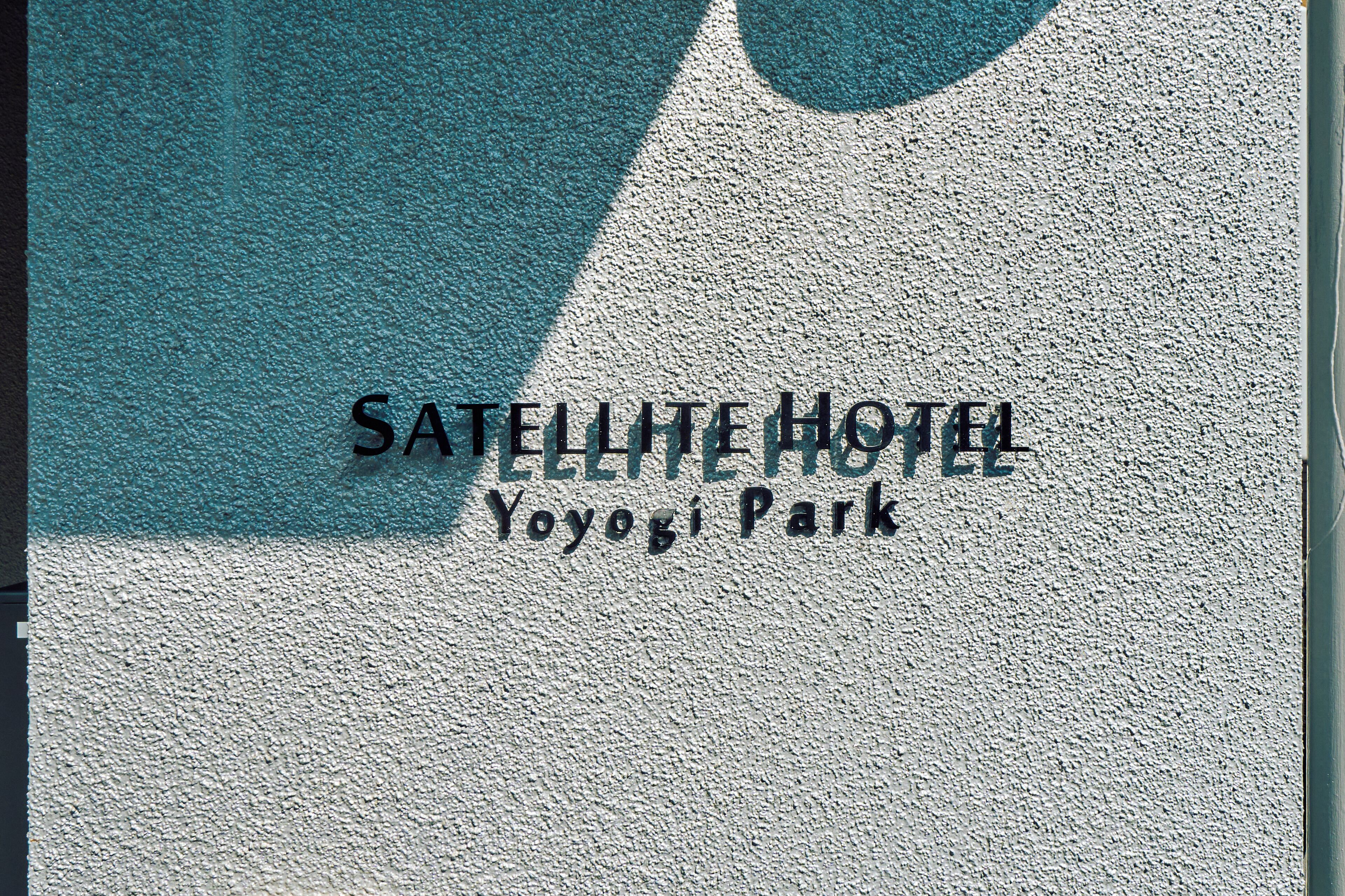A textured wall with the text "SATELLITE HOTEL" and "Yoyogi Park" indicating the hotel's name and location.