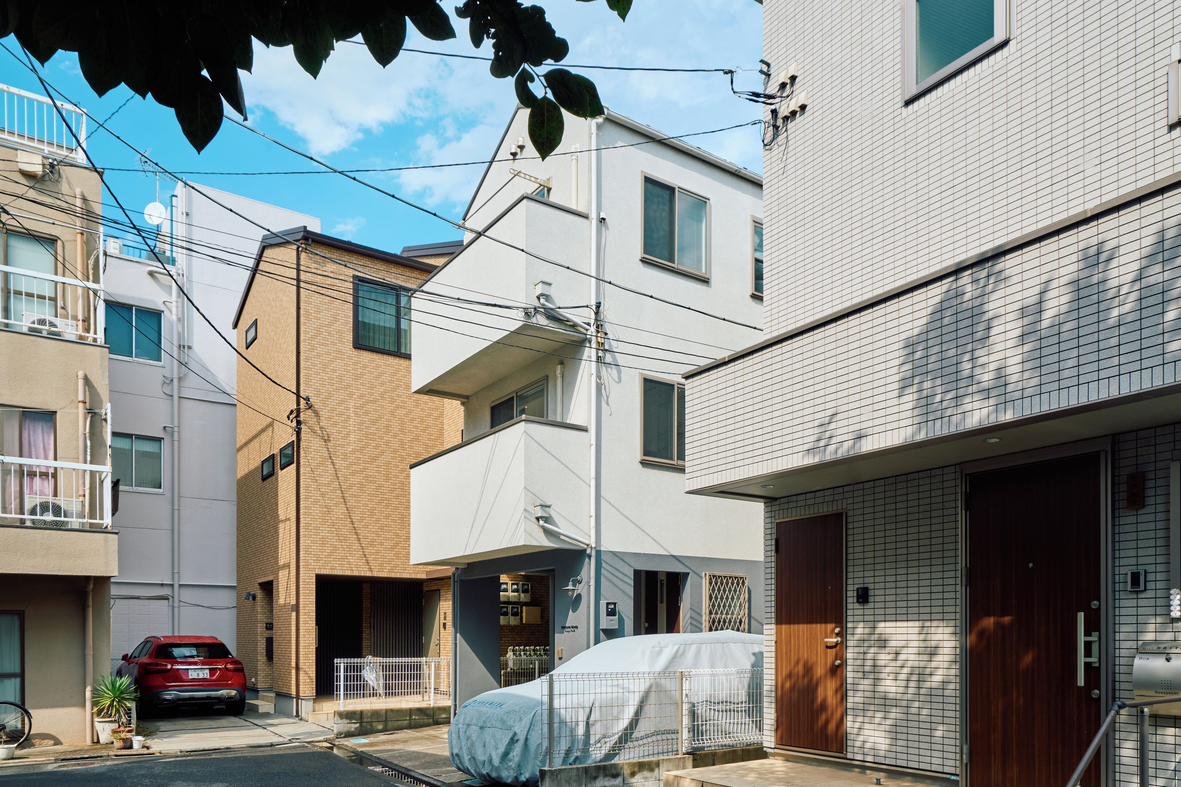 A residential building with a covered carport, a red car parked in front, and a bicycle to the left.