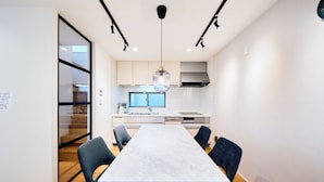 A modern kitchen with a large island, a dining area with a marble table, and a view of the living area through a glass door.