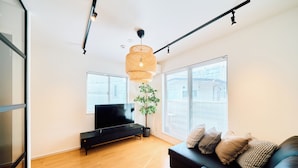 A modern living room with a flat-screen TV, a black sofa, and a large window with blinds.