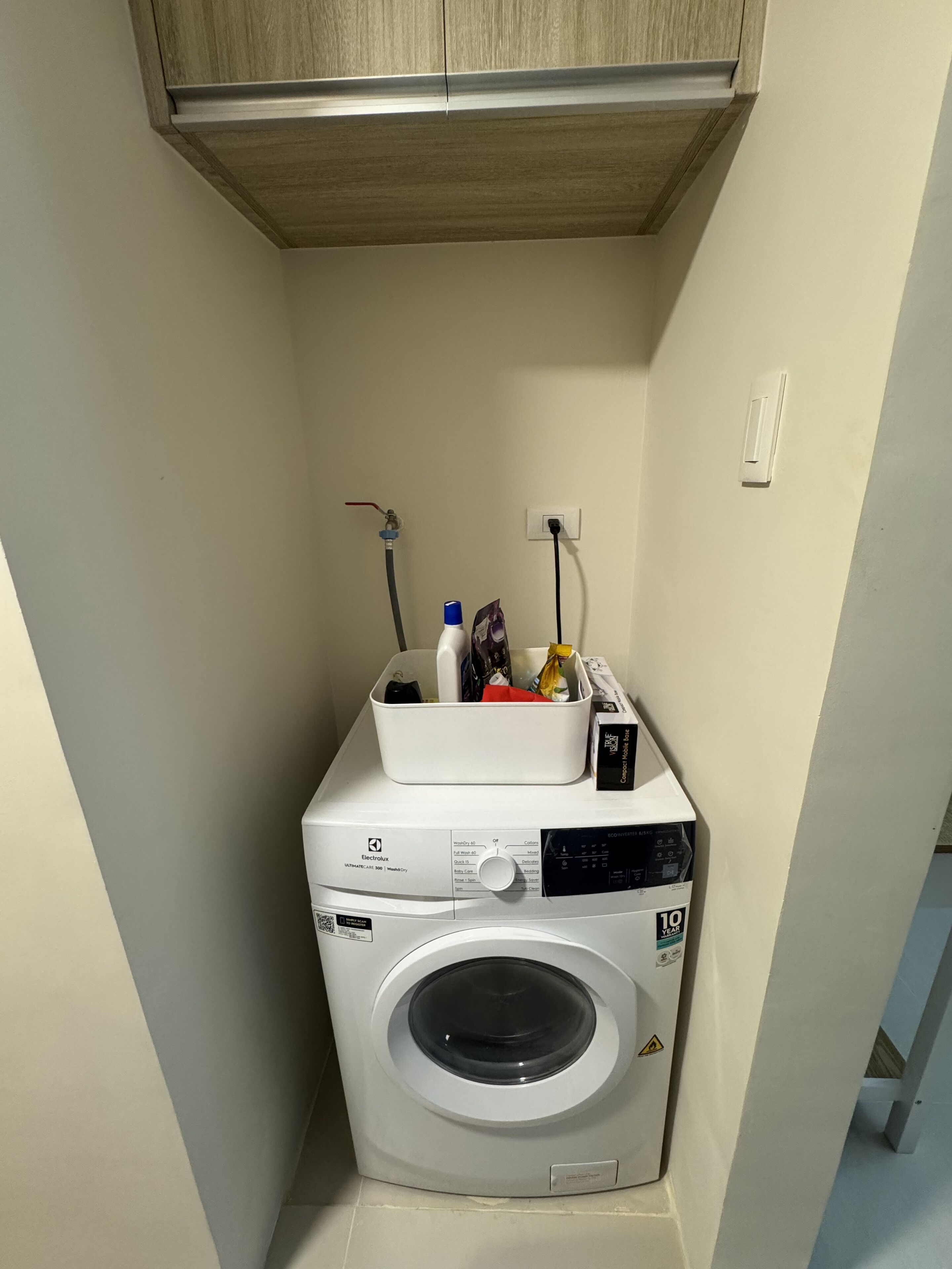 Une petite buanderie équipée d’un lave-linge à chargement frontal, d’un étendoir et d’un petit meuble de rangement placé au-dessus.