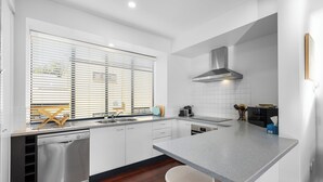 Una cocina moderna con armarios blancos, lavavajillas de acero inoxidable, encimera gris y taburetes de madera.