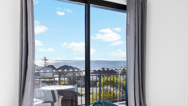 Habitación de hotel con un ventanal grande, una cama con una toalla enrollada y vistas a un edificio y zonas verdes.