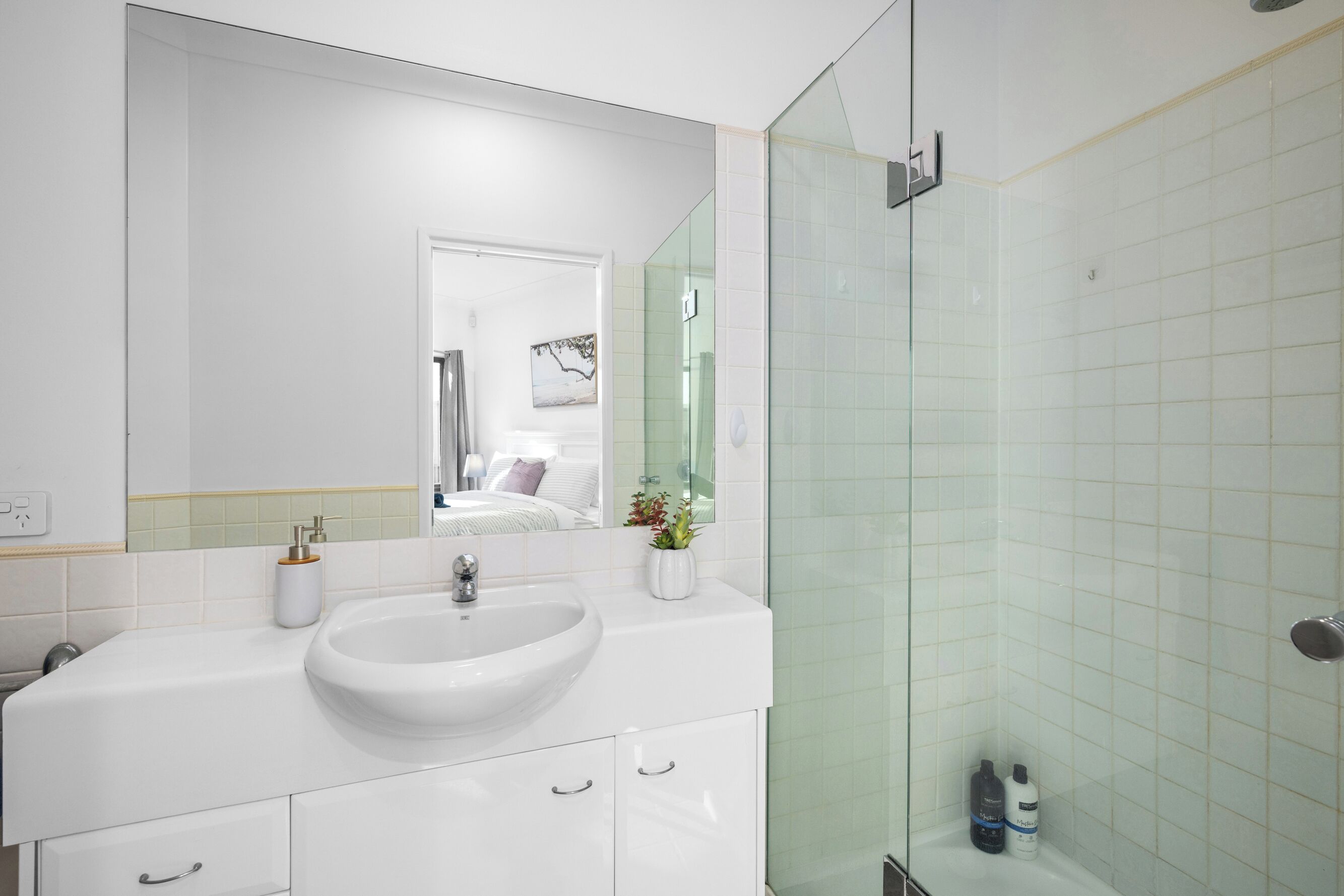 A modern bathroom with a white sink, a large mirror, and a glass shower enclosure.