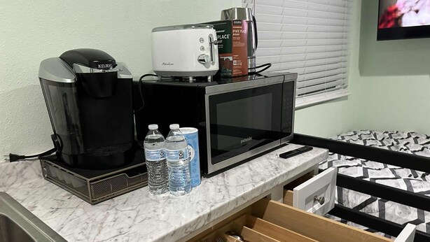 Un angolo cottura con macchina del caffè, forno a microonde, tostapane e bottiglie d'acqua.