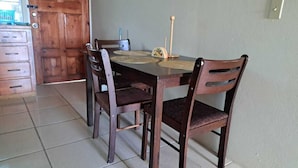 Un comedor con una mesa de madera y cuatro sillas, una puerta de madera y un suelo de baldosas.