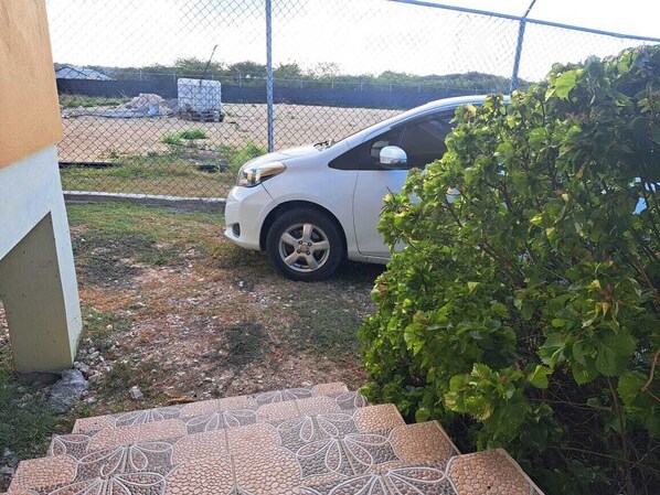 A parking area with a white car, a paved entrance with a decorative pattern, and a green bush.