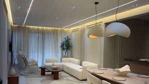 A modern living room with a sofa set, a dining table with chairs, and a large flat-screen TV.