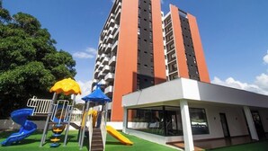A playground with slides and climbing structures, a building with a modern design, and a clear blue sky.