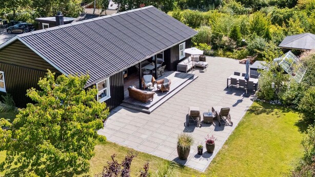 Una casa moderna con un amplio patio que cuenta con mobiliario exterior y una zona de estar cubierta.