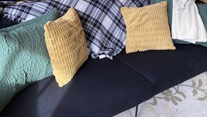 Interior de una cabaña de madera con una cama en el altillo, una ventana con vistas a árboles y una zona de estar acogedora con una manta y almohadas a cuadros.