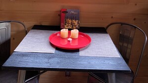 Ein Holzhütten-Innenraum mit zwei Fenstern, einem Schachbrett und Kerzen auf einem Tisch.