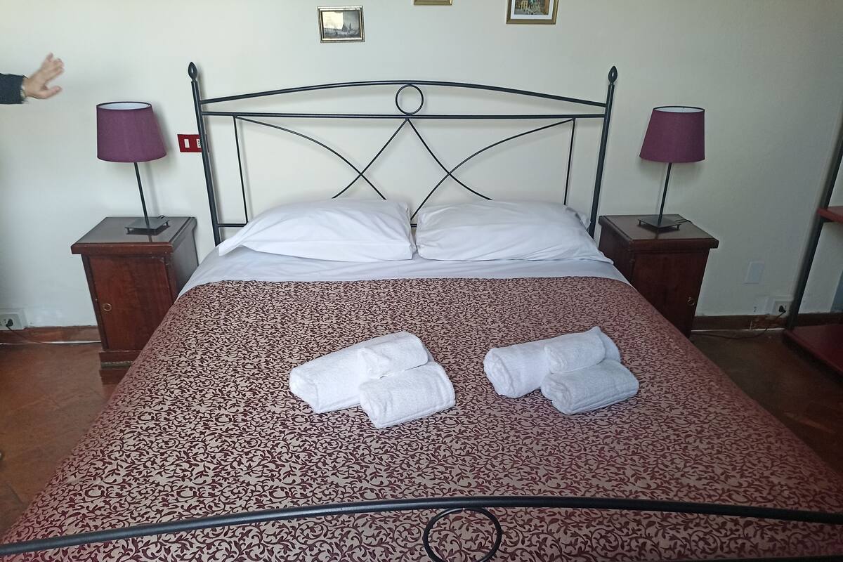 A neatly made bed with a patterned bedspread, two bedside tables with lamps, and a hand reaching towards the bed.