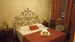 A neatly made bed with a patterned bedspread, a decorative headboard, and a small table with a lamp and flowers.