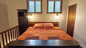Une chambre à coucher avec un lit, deux fenêtres, une commode et un appareil de climatisation.