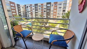 A balcony with two wicker chairs and a small round table, overlooking a residential area with multiple apartment buildings.