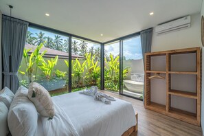 Une chambre d’hôtel moderne avec un grand lit, une armoire en bois et une vue sur une végétation tropicale et des palmiers.