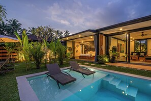 Une maison moderne dotée d’une piscine, de deux chaises longues et d’un espace patio agrémenté de plantes.