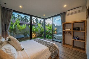 Un dormitorio con una cama grande, un armario de madera y vistas a un jardín con palmeras.