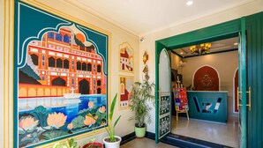 A hotel lobby with a large mural of a traditional building, potted plants, and a reception desk. - Zostel Agra (Agra)