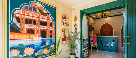 A hotel lobby with a large mural of a traditional building, potted plants, and a reception desk.
