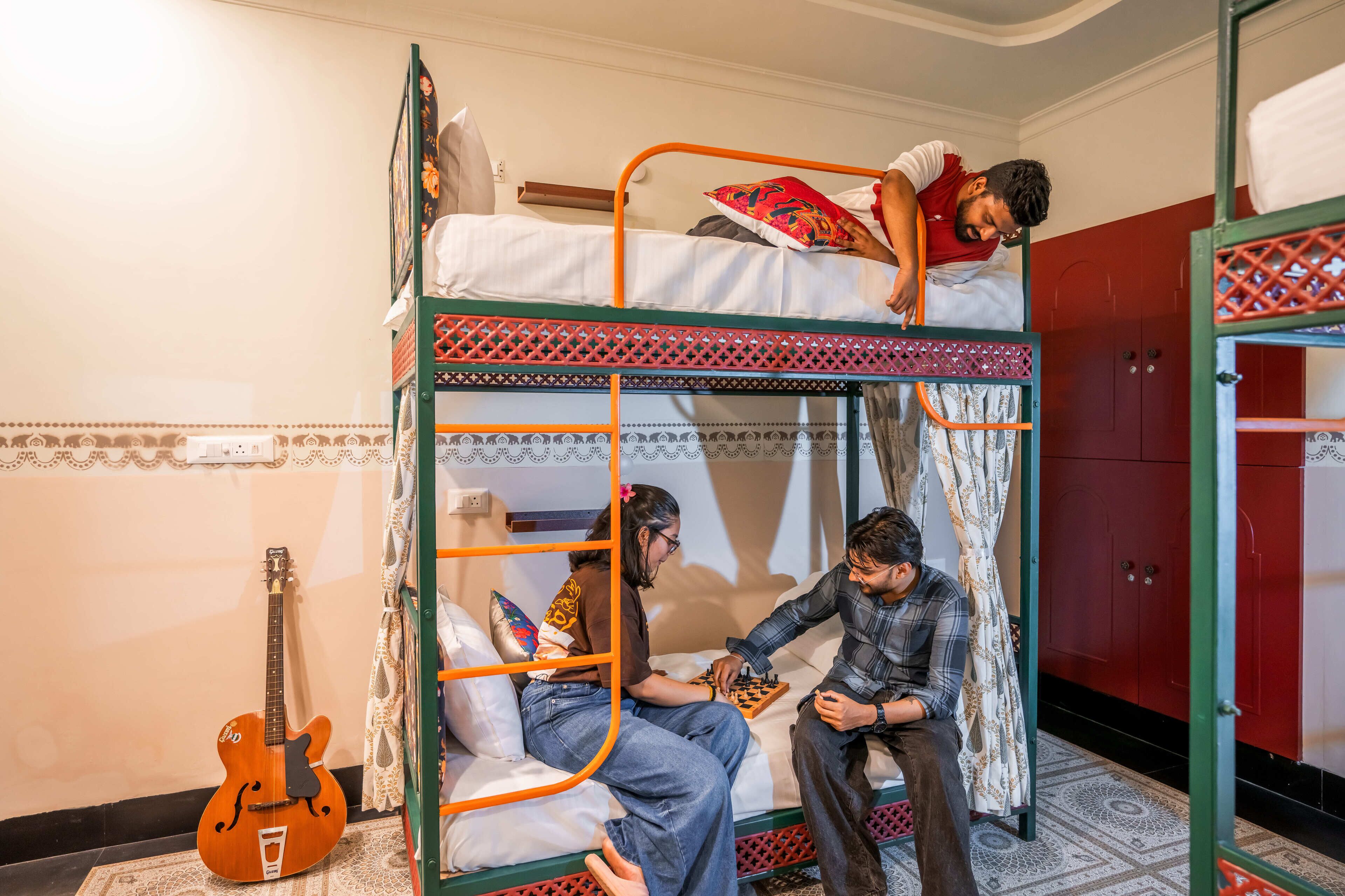 Dormitorio con literas, una guitarra, un tablero de ajedrez y una alfombra estampada.
